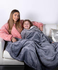 Two people sitting on a white couch, covered with grey and pink Ribbon RI014 fleece blankets, smiling at the camera.
