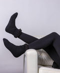 Two people wearing black socks and black pants relax with their legs up on a white chair against a plain background, showcasing the Ribbon RI016.