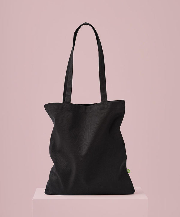 The Nutshell Premium organic canvas shopper long handle is shown upright on a light pink rectangular plinth, set against a solid pale pink background.