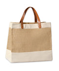 The Bags tote features tan canvas sides and bottom, hessian-style front and back, plus two brown leather handles with metal rivets. The empty bag stands upright against a white background.