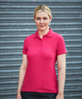 Person with blonde hair wearing a pink RX01F polo shirt from ProRTX stands in front of a gray corrugated metal background.