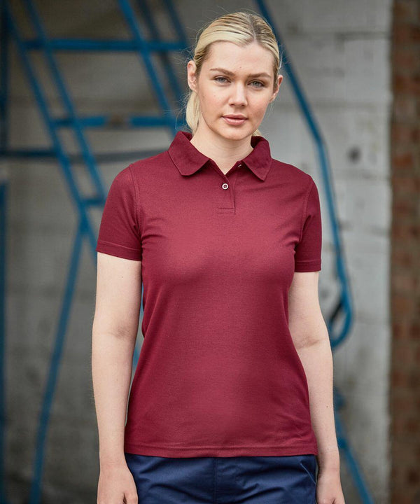 A woman wearing a short-sleeved maroon ProRTX RX05F shirt stands in front of a blue metal structure and a brick wall.