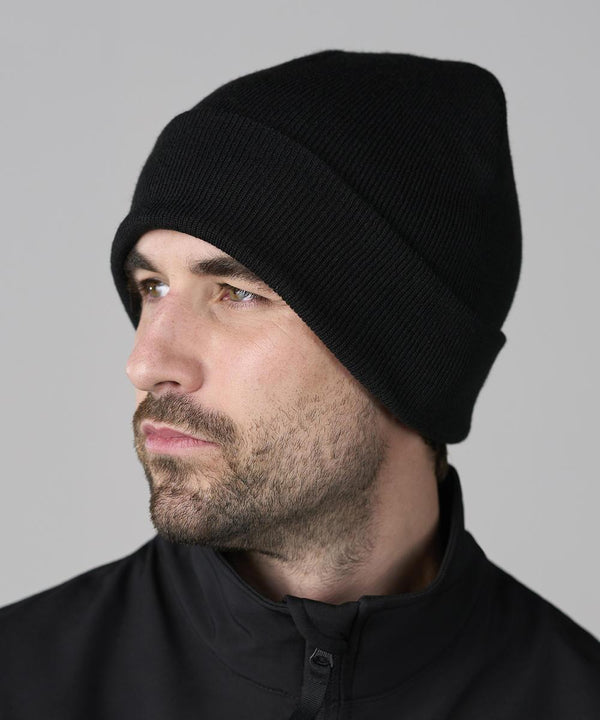 A man with a short beard and moustache wears a ProRTX Pro cuffed beanie and a black zip-up jacket, looking to the left against a plain grey background.