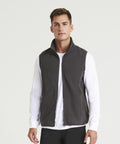 A man stands wearing a dark grey ProRTX RX405 zip-up vest over a white long-sleeve shirt and black pants, facing the camera.