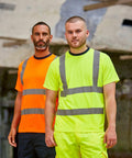 Two men stand side by side, wearing high-visibility shirts: one in orange with reflective stripes and the other in neon yellow with reflective stripes. Both are sporting the RX720 from ProRTX. A blurry industrial background is visible.