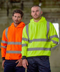 Two men stand side by side wearing ProRTX RX740 high-visibility hoodies; one in bright orange and the other in neon yellow. The background is an industrial setting.