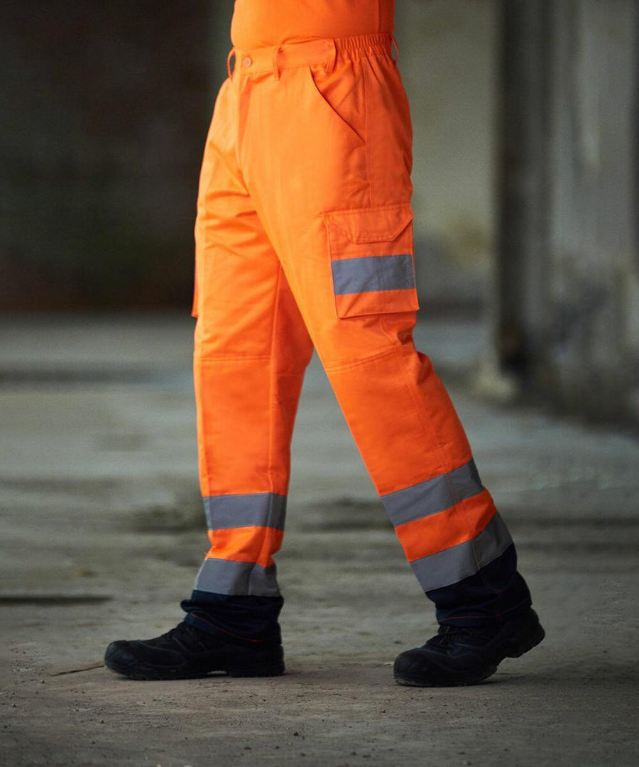Person wearing ProRTX RX760 high-visibility work trousers with reflective stripes and black shoes, walking indoors.