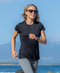 A person wearing Spiro S253F and a black T-shirt is jogging outdoors by the water, with a mountainous landscape in the background.