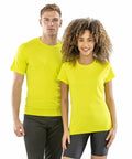 Two people, one with short blonde hair and the other with curly hair, are wearing matching bright yellow Spiro S253M T-shirts. The person with curly hair is smiling, while the other maintains a neutral expression.