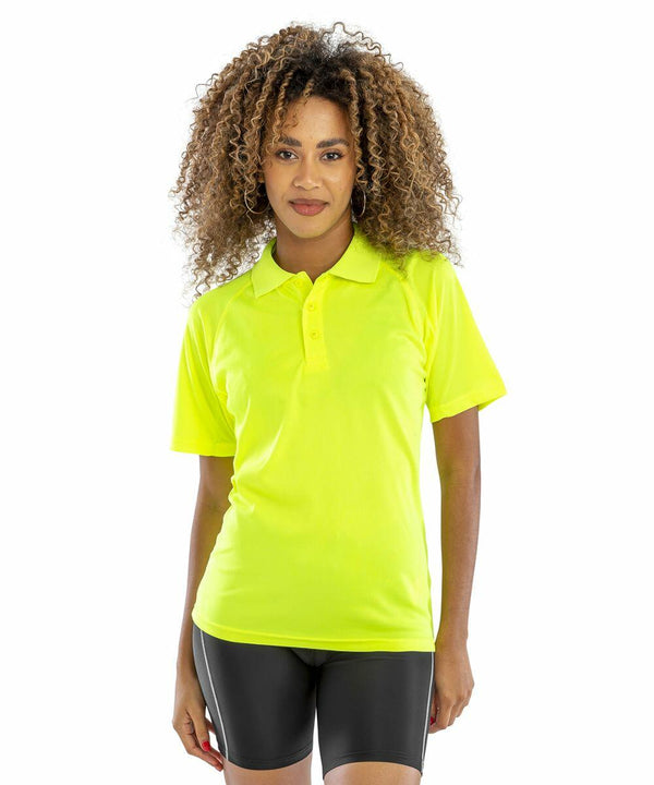 A person with curly hair is wearing a bright yellow Spiro S288X polo shirt and black cycling shorts, standing against a plain white background.
