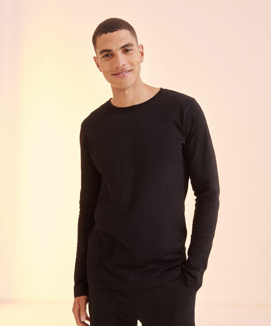 A person wearing an SF SF124 black long-sleeve shirt stands against a light-colored background, smiling and with one hand in their pocket.