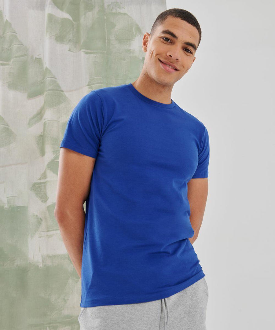 A person in a blue t-shirt and gray pants stands against a light-colored background, smiling and looking at the camera with an SF130 by SF.