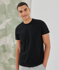 A man wearing a black t-shirt and light-colored pants is standing and smiling in front of an SF SF140 light green and white textured background.