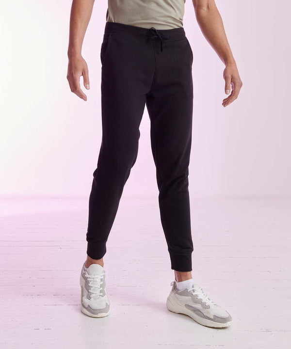 Person wearing black jogger pants, a beige t-shirt, and SF SF425 white sneakers standing on a light-colored floor.