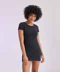 Person with curly hair wearing a black short-sleeved SF SK257 dress stands against a plain background, smiling.