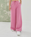 A person wearing pink wide-leg pants and white SK431 sneakers by SF stands on a white floor with a green and white textured background.