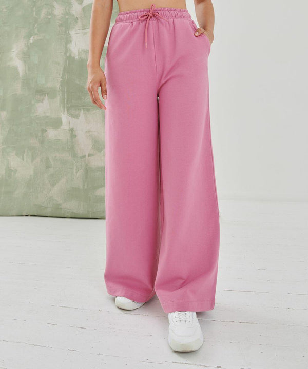 A person wearing pink wide-leg pants and white SK431 sneakers by SF stands on a white floor with a green and white textured background.