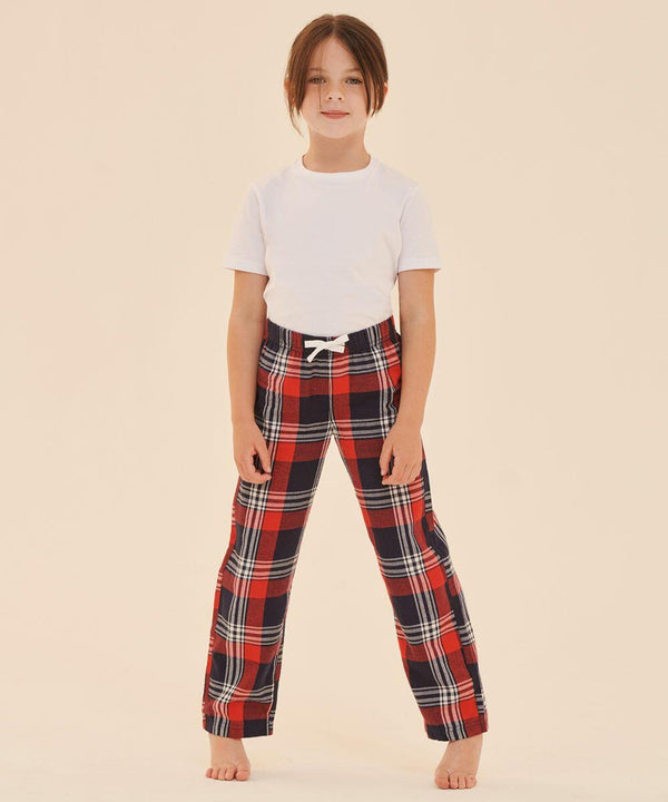A child with long hair stands barefoot, wearing a white t-shirt and red and black plaid SF Minni SM083 pajama pants against a plain beige background.