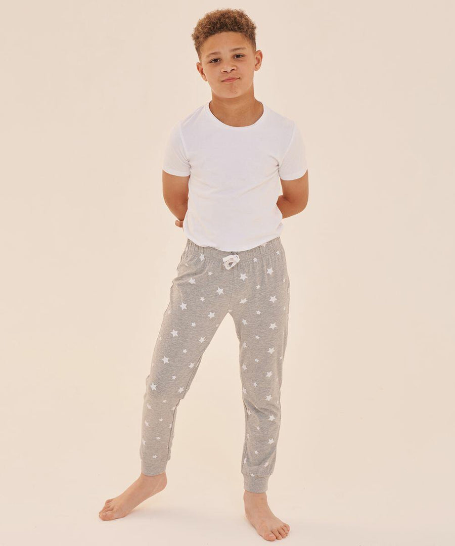 A young boy stands barefoot, wearing a white t-shirt and grey SF Minni SM085 pajama pants with a white star pattern, against a plain light background.