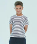 A young boy with curly hair stands against a plain background, wearing a black and white striped SM202 T-shirt by SF Minni and dark pants, with his hands behind his back.