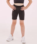 A person standing with hands on hips, wearing a black top and black SF Minni SM427 shorts, white socks, and white sneakers, against a plain light background. The person's torso is not visible.