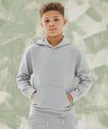 A young person with short curly hair stands against a textured green background, wearing an SF Minni SM531 light gray hoodie with hands in the front pocket.