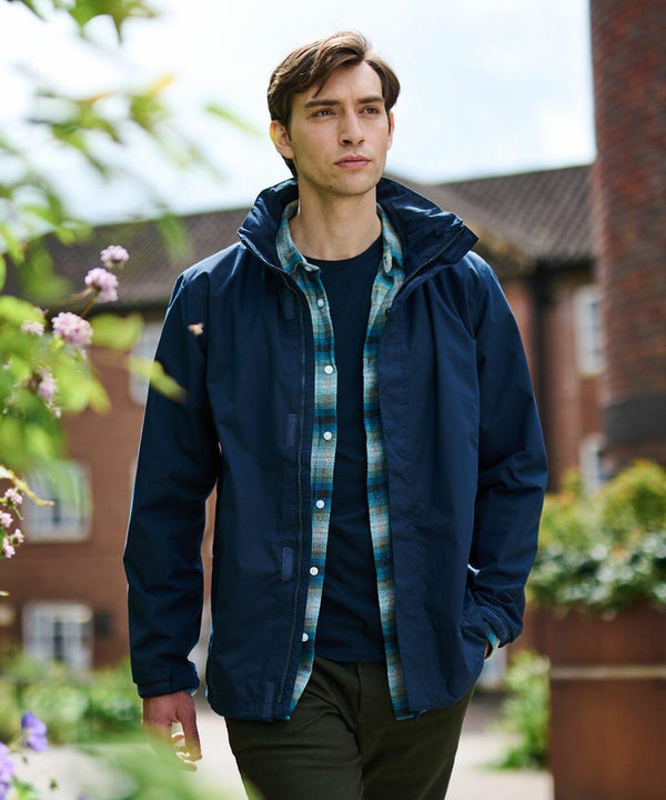 A person wearing a Regatta SN100 jacket over a checkered shirt walks in an outdoor setting with buildings in the background.