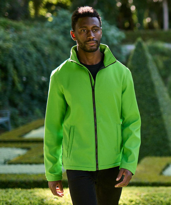 A man wearing a bright green Regatta SN130 walks outdoors in a garden setting with manicured hedges and greenery in the background.