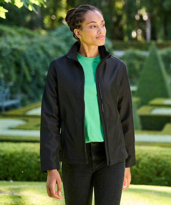 A person wearing a green shirt and a Regatta SN131 jacket stands in an outdoor garden with manicured hedges.