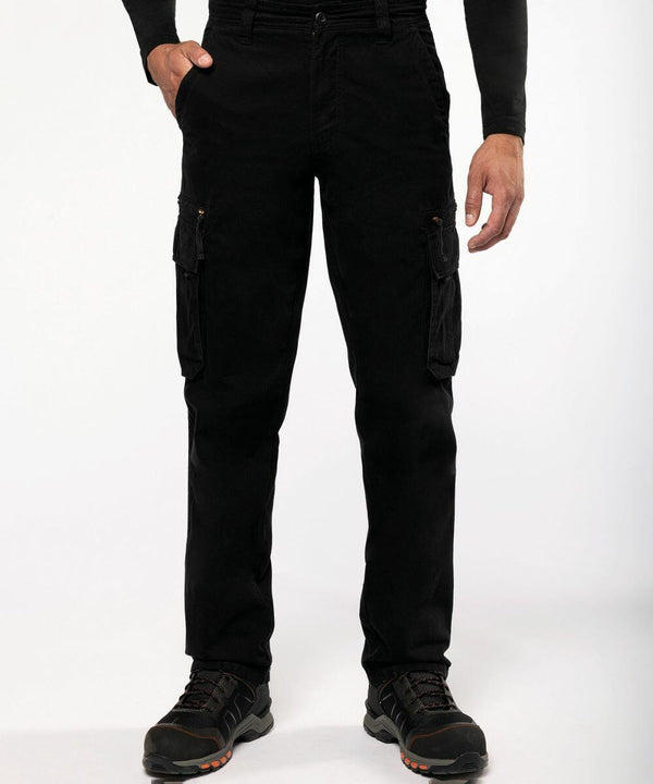A person is wearing black cargo pants with multiple pockets, a black long-sleeve top, and Kariban SP105 shoes with orange accents. The background is plain white.
