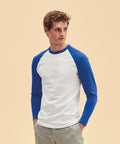 A person wearing a long-sleeve Fruit of the Loom SS028 shirt with a white torso and blue sleeves, and light-colored pants, stands against a neutral background.