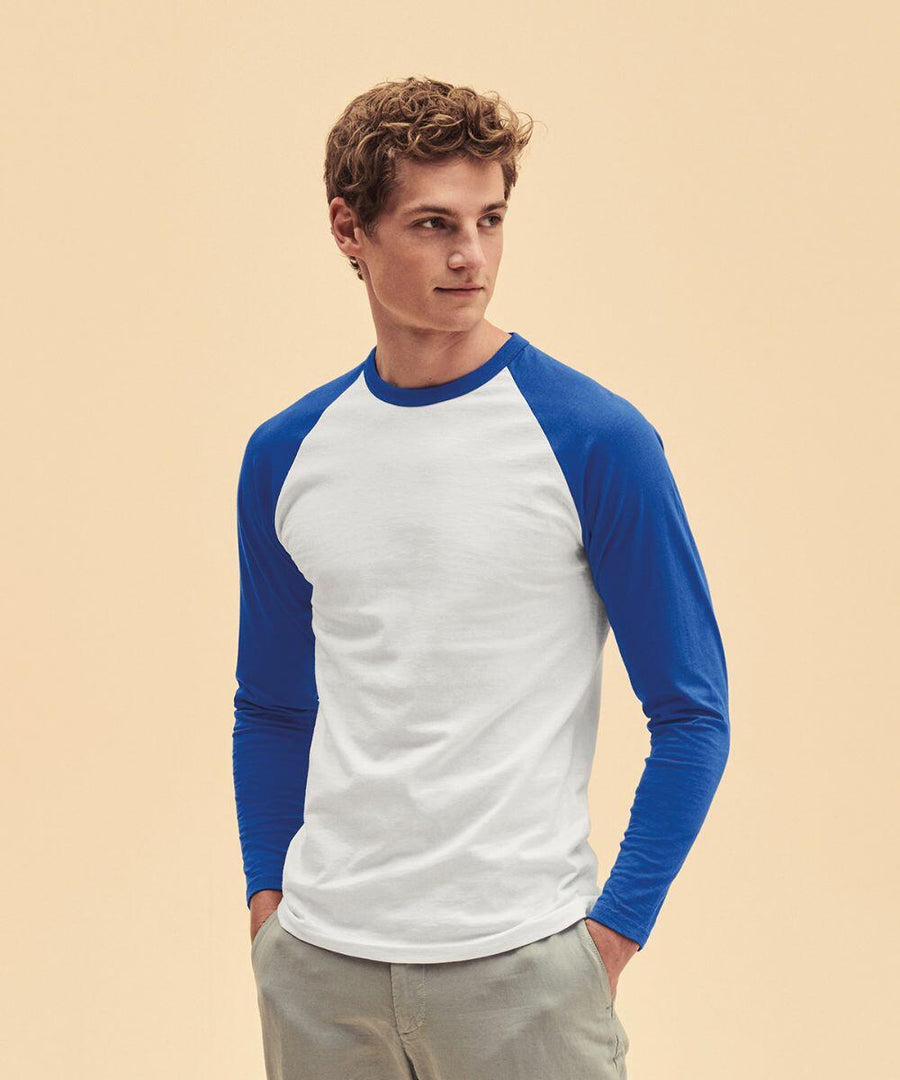 A person wearing a long-sleeve Fruit of the Loom SS028 shirt with a white torso and blue sleeves, and light-colored pants, stands against a neutral background.