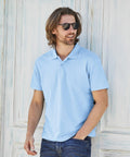 A man with long hair wearing sunglasses and a light blue Fruit of the Loom SS029 stands against a wooden background with a hand in his jeans pocket.