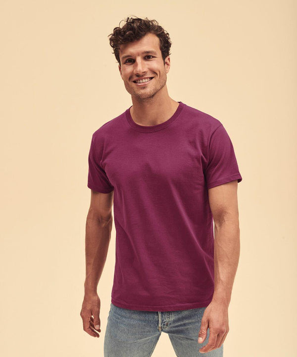 A man stands against a beige backdrop, smiling, wearing a Fruit of the Loom SS030 purple t-shirt and blue jeans.