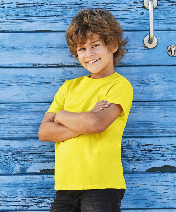 Child with curly hair wearing a yellow Fruit of the Loom SS088 shirt and black pants stands with arms crossed in front of a blue wooden wall.