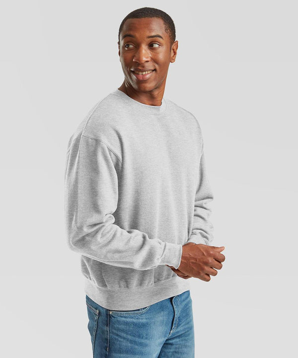 A man in a light grey Fruit of the Loom Supercotton sweatshirt and blue jeans stands against a plain white background, looking to his left with a slight smile.