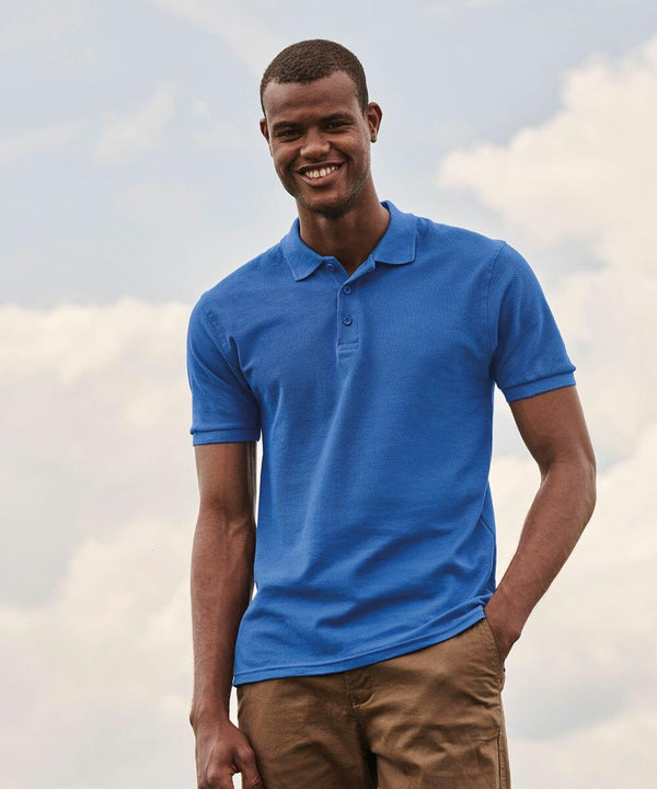 A man in a blue SS255 Fruit of the Loom shirt and brown pants smiles while standing outdoors against a cloudy sky.
