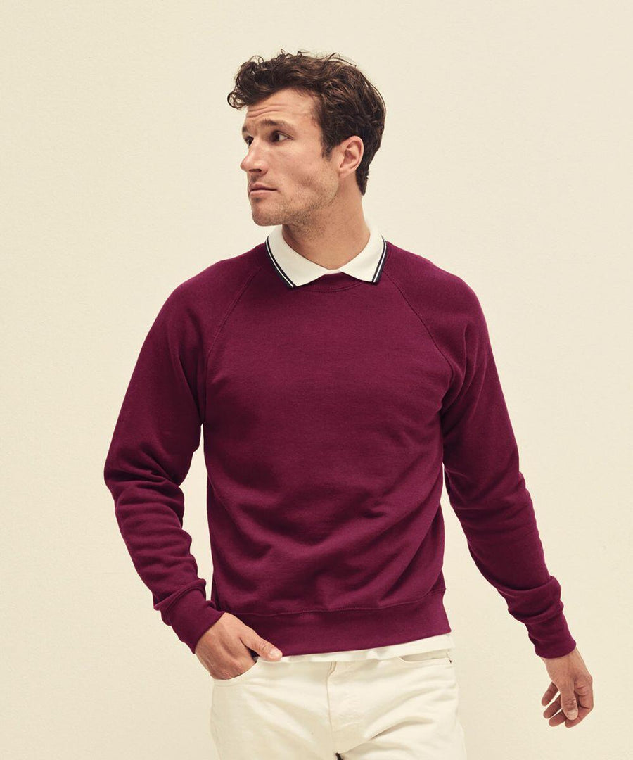 A man in a burgundy Fruit of the Loom SS270 sweatshirt and white collared shirt looks to the side. He has short, curly brown hair and stands against a plain, light-colored background.