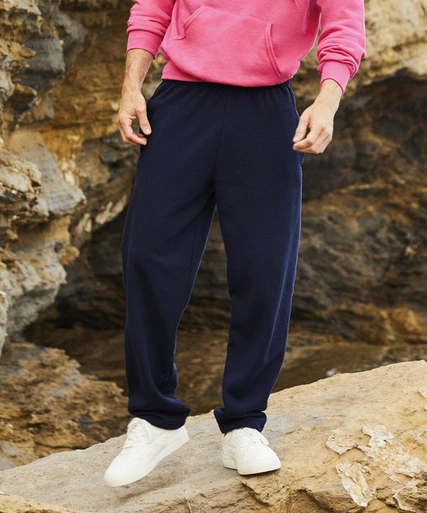 Person standing on rocky terrain wearing navy blue sweatpants, a pink Fruit of the Loom SS324 hoodie, and white sneakers, torso not visible.