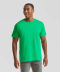 A man is standing and smiling slightly, wearing a bright green SS422 t-shirt and gray pants from Fruit of the Loom. The background is plain white.