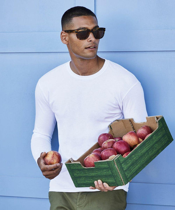 A man in sunglasses and a white shirt holds a Fruit of the Loom SS433 box filled with red apples and one apple in his other hand in front of a blue wall.