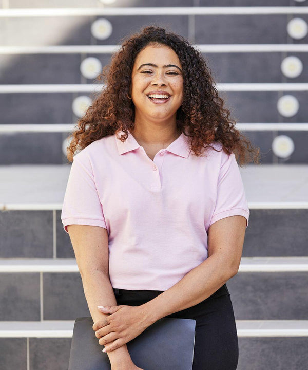 A smiling person with curly hair in a pink Fruit of the Loom SS505 shirt holds a black folder while standing in front of steps.