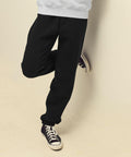 Person wearing black SS805 pants and black sneakers with white soles, leaning against a wall.