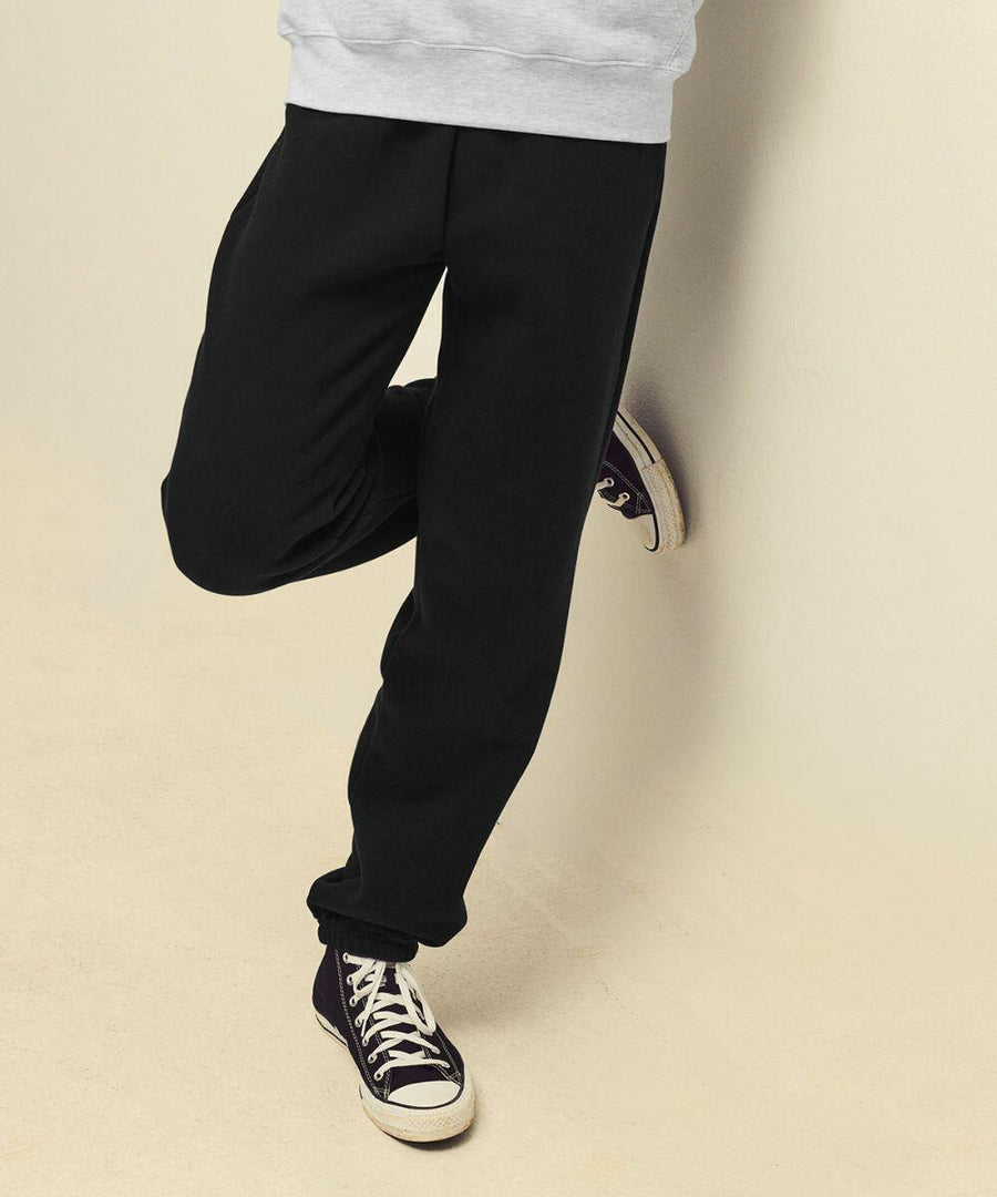 Person wearing black SS805 pants and black sneakers with white soles, leaning against a wall.