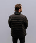 A person with brown hair wearing a black Stormtech ST143 puffer jacket stands facing away against a plain grey background.