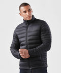 A man wearing a black, quilted Stormtech ST154 jacket with a high collar and zipper front stands against a plain, white background.