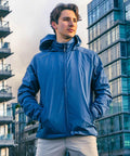 Young man in a blue Stormtech ST166 stands confidently outdoors with modern buildings in the background.