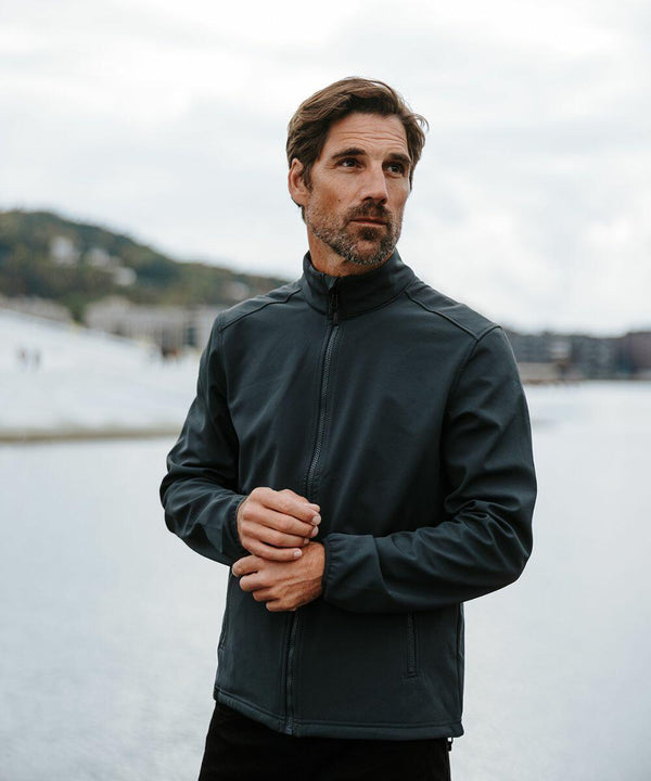 A man with a beard stands outdoors near water, wearing a dark Stormtech ST200 zip-up jacket and looking to his left.