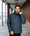 A man with a beard and short hair wearing a dark blue Stormtech ST214 puffer jacket stands in an outdoor covered walkway, adjusting his collar.