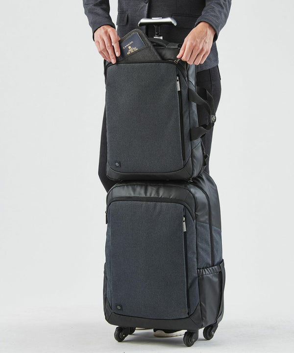 Person holding a passport and a backpack, with a Stormtech ST222 bag on wheels underneath.